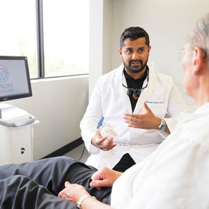 Dr. Shroff holding a dental model and explaining tooth extraction costs to a patient