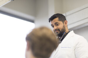 A headshot photo of a dentist, with a blurred patient in the foreground